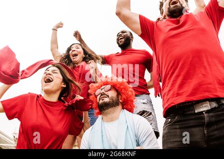 Football fans celebrating victory at stadium with disappointed rival supporter Stock Photo