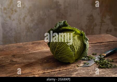 Fresh ripe Savoy cabbage and knife placed on wooden table in rustic kitchen Stock Photo