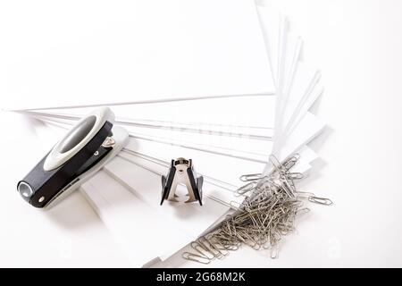 Photograph of some fan-shaped sheets of paper, a stapler, a staple extractor and some paper clips on a white background.The photo has free space to pu Stock Photo