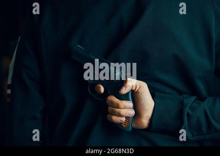 Man holds firearm behind his back. Person ready to attack with hand gun. Revolver in men's hand. Stock Photo