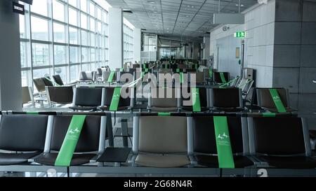 June, 2021:  Frankfurt airport, transit zone, Terminal sitting area, distance marked by green tape. Row of empty lounge seats by a window, day light. Stock Photo