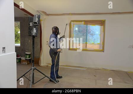 a tradesman using airless spray equipment to paint a top coat on the walls of a commercial building Stock Photo