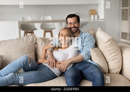Portrait of smiling young couple hugging sitting on comfortable couch Stock Photo