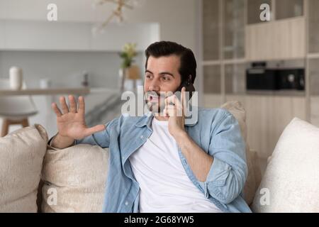 Smiling man talking on phone sitting on couch at home Stock Photo