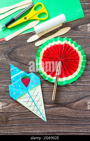 Paper Fan watermelon and origami paper ice cream, summer toy wooden sticks on a wooden table. Childrens art project, handmade, crafts for children. Stock Photo