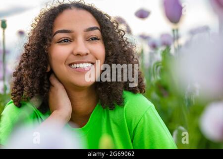 Mixed race beautiful African American biracial girl teenager female young woman wearing green t shirt in field of pink or purple flowers poppies at sm Stock Photo