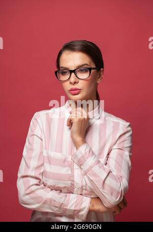 Thinking woman wearing glasses and casual shirt on red background Stock Photo
