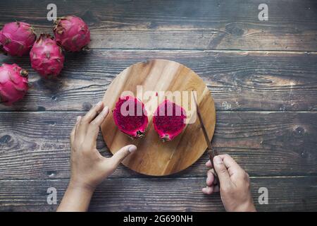 young man cutting a dragon fruit on a chopping board. Stock Photo