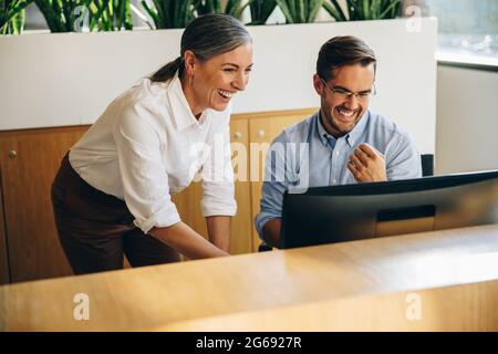 Smiling colleagues working together on project. Male and female business professionals using computer at office. Stock Photo