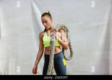 Fit woman in sportswear doing battle rope workout. Female athlete exercising using battle rope. Stock Photo
