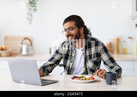 Cheerful middle-eastern guy having snack while working from home Stock Photo