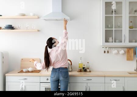 Back view woman select mode on cooking hood in kitchen Stock Photo