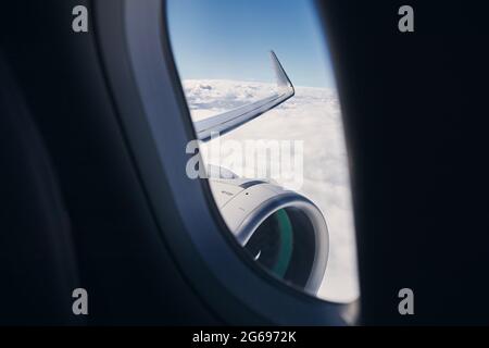 View through airplane window on wing with engine. Plane during flight above clouds.