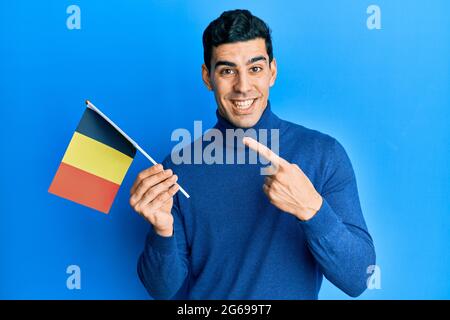Handsome hispanic man holding belgium flag smiling happy pointing with hand and finger Stock Photo