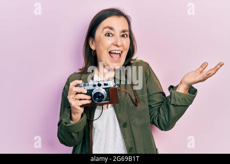 Middle age hispanic woman holding vintage camera celebrating achievement with happy smile and winner expression with raised hand Stock Photo