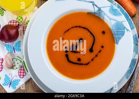 Pumpkin soup watered with pumpkin oil, in a plate with a picture. View from above. On the table next to the plate are various vegetables, a glass of j Stock Photo