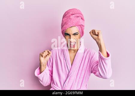 Young man wearing woman make up wearing shower towel on head and bathrobe dancing happy and cheerful, smiling moving casual and confident listening to Stock Photo