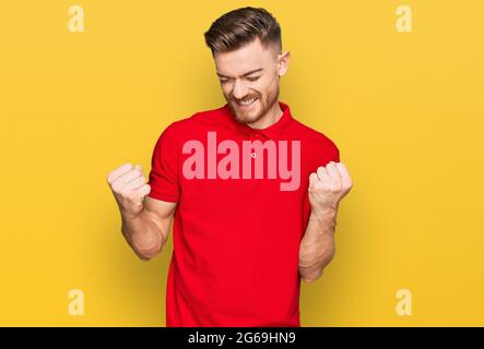 Young redhead man wearing casual clothes very happy and excited doing winner gesture with arms raised, smiling and screaming for success. celebration Stock Photo