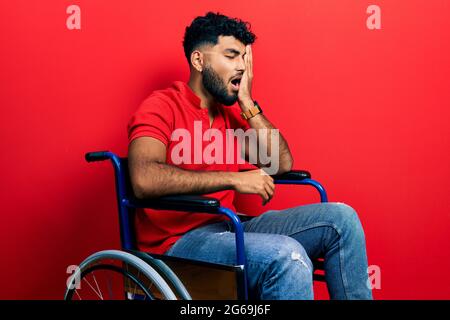 Arab man with beard sitting on wheelchair yawning tired covering half face, eye and mouth with hand. face hurts in pain. Stock Photo