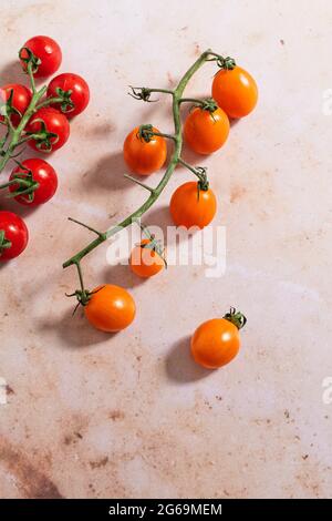 Red and orange vine cherry tomatoes on a pink marble backdrop Stock Photo