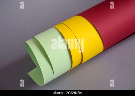 Rolled-up colored thick paper of red, yellow and green colors, on gray background. Close-up. Selective focus. Stock Photo