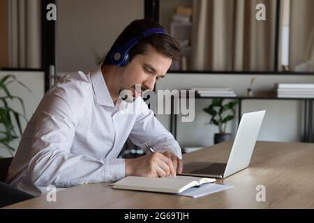 Employee in headphones taking notes, watching webinar in office Stock Photo