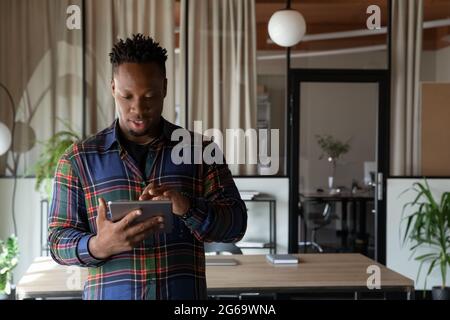 Confident African American businessman using tablet, standing in office Stock Photo