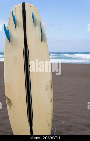 Detail shot of a surfboard stuck in the sand in front of the sea. Stock Photo
