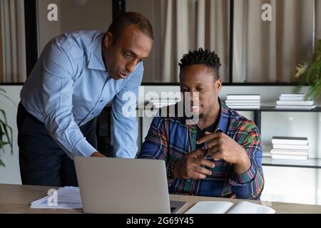 African American mentor teaching intern, pointing at laptop screen Stock Photo