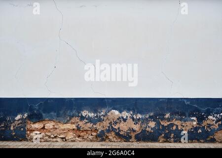 Old whitewashed lime wall with dark blue skirting board and peeling paint, traditional architecture in La Mancha, Spain Stock Photo