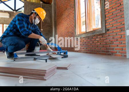 Asian artisan tiler at construction site, worker cuts a large slab of tile during the construction of a house, floor tile cutting equipment Stock Photo