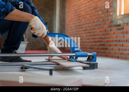 Close up hand of an artisan tiler at construction site, worker cuts a large slab of tile during the construction of a house. Stock Photo