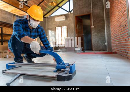 Select focus floor tile cutting equipment, Asian artisan tiler at construction site, worker cuts a large slab of tile during the construction of a hou Stock Photo