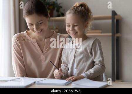 Happy preteen girl preparing school assignment with help of mother Stock Photo