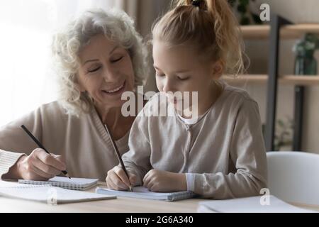 Friendly old female private tutor interact with preteen girl pupil Stock Photo