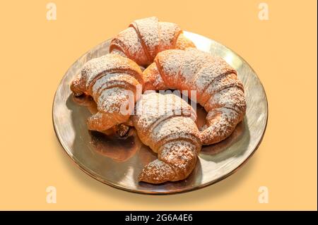 Croissant brioches with icing sugar on silver plate isolated on orange background Stock Photo