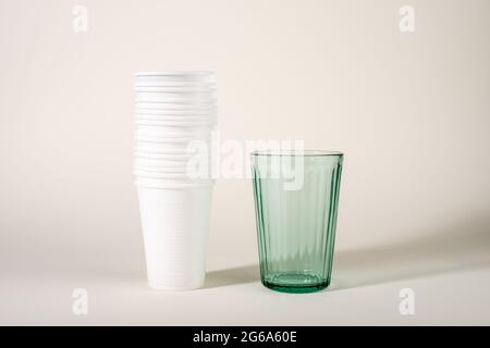 Glass and stack of plastic cups. Glass or plastic. Reusable versus disposable. Zero waste concept. Stop plastic pollution. Stock Photo
