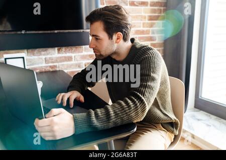 Serious mid aged man working on laptop computer from home, taking notes Stock Photo