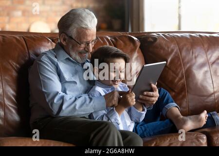 Happy gen Z grandkid and 70s grandfather using tablet Stock Photo