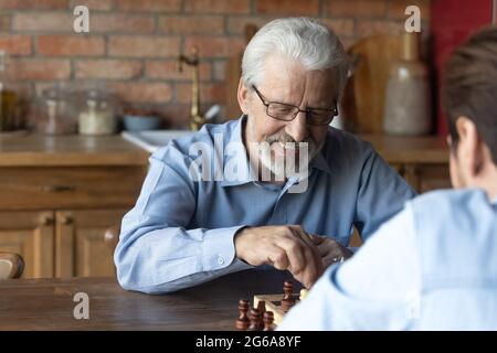 Happy 70s father playing chess and talking to grown son Stock Photo