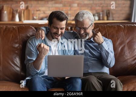 Happy excited grown son and mature 70s father using laptop Stock Photo