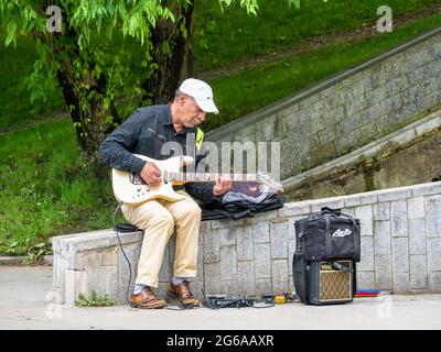 Bucharest, Romania - 06.04.2021: Senior street artist musician sitting on a bench in the park and playing at an electric guitar Stock Photo