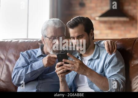 Grown son teaching elderly 70s dad to use mobile app Stock Photo