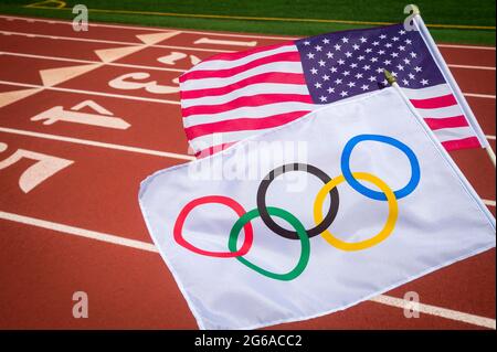 MIAMI, USA - AUGUST, 2019: An Olympic and American flag flutter together above a red athletics track. Stock Photo