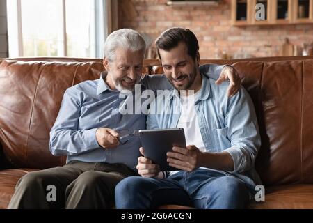 Happy grown son teaching senior father to use tablet Stock Photo