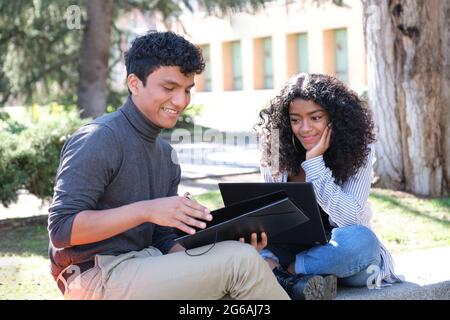 Two latin students studying together sitting on a bench outdoors. University life at campus. Stock Photo