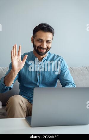 Portrait of indian business man waving hand to online interlocutor using laptop Stock Photo