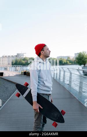 Hipster guy with longboard on city bridge. Trendy man hipster skateboarder hold skateboard in hand Stock Photo