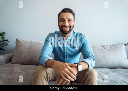 Portrait of indian man toothy smiling to camera sitting on sofa webcam view Stock Photo