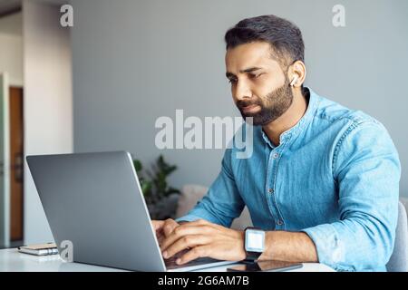 Portrait of handsome young indian man using laptop and earphone at home office Stock Photo